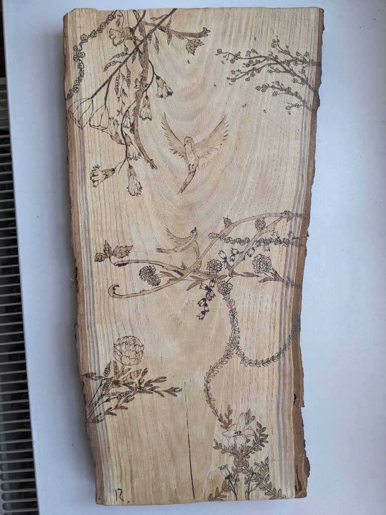 Pyrogravure oiseau en vol autour de branches de fleurs